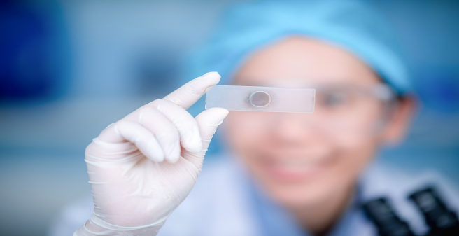 Lächelnder Mensch guckt durch Objektträger