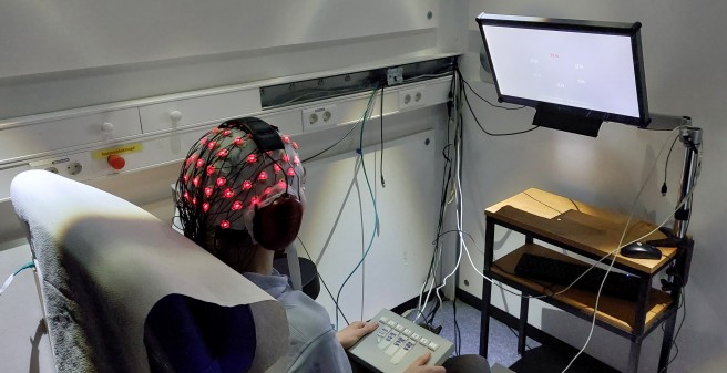 Mensch sitzt fur EEG-Messung mit Elektroden auf dem Kopf in Untersuchungsraum und guckt auf Bildschirm